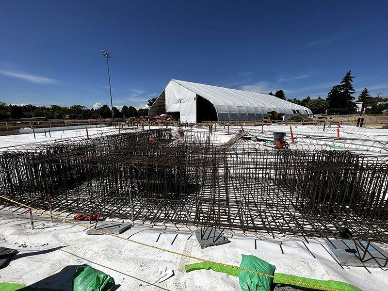 rebar formed into tall grids sits in foreground on top of a white material. a large tent is in the background