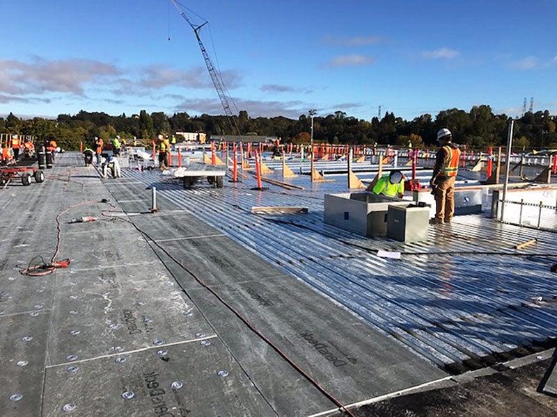 a large flat surface has a crane in the background, workers spread around, and a lot of orange construction standards