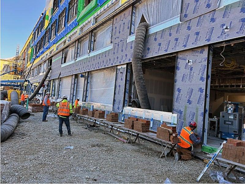 part of a larg building with openings for windows. workers have stacks of bricks next to them as they install them