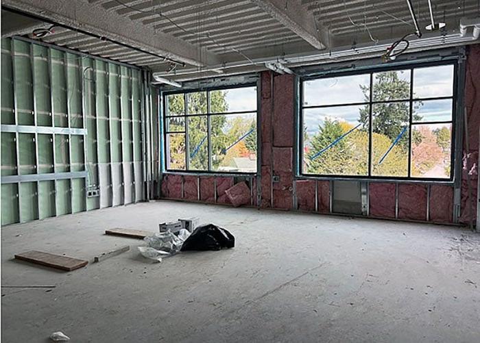 a room with two large windows is under construction with pink insulation around the windows and metal framing on the right wall