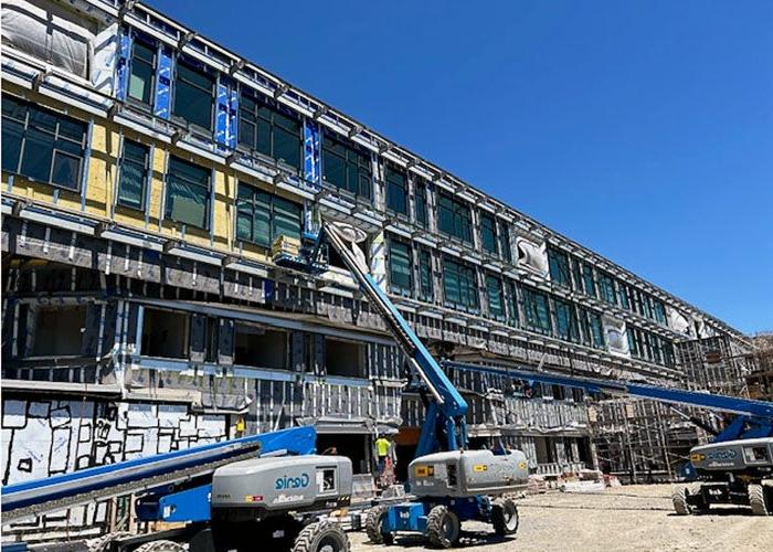 part of a long 4-story building under construction with a lift truck and people working on the windows